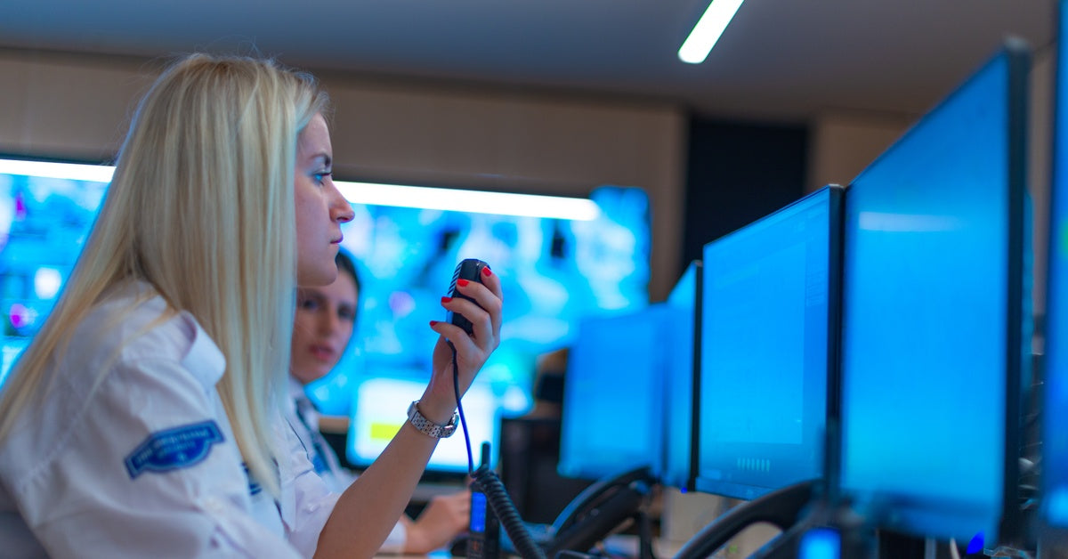 A couple of women work in a data center with many monitors in front of them and large screens on the wall behind them.