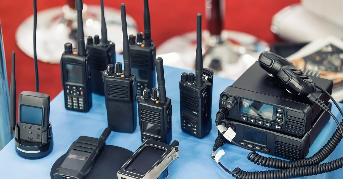 A variety of two-way radio equipment is displayed on a small table with a blue tablecloth at a tech convention.