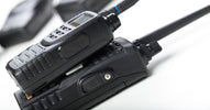 Two different types of two-way radios are stacked on top of each other on a white table with more radios in the background.