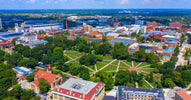 An aerial view of a large college campus shows intersecting paved walkways in a green space with a stadium in the distance.